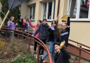 Uczniowie klasy 4 wraz z nauczycielem zaangażowani w prace porządkowe wokół szkoły.