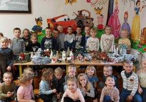 Dzieci stoją przy stole z dekoracjami świątecznymi