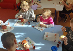 Dzieci malują farbami pączki z papieru.