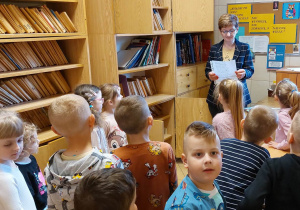 Dzieci słuchają zagadek czytanych przez Panią bibliotekarkę