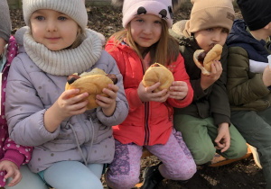 Dzieci siedzą na ławeczce, jedzą kiełbaskę z ogniska