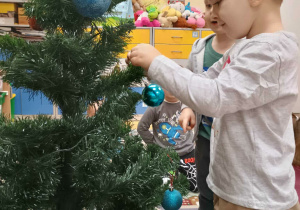 Chłopiec zawiesza na choince bombkę