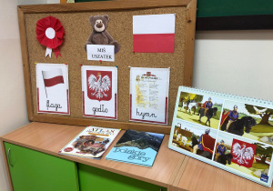 Na zdjęciu widać gazetkę, na której widnieją polskie symbole narodowe, Miś Uszatek oraz kotylion. Obok znajdują się książki oraz ilustracje związane z Polską.