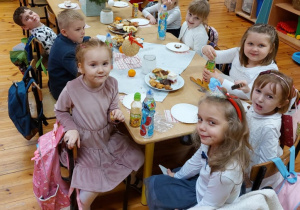 Na zdjęciu widać grupę dzieci wraz z Panią, którzy siedzą przy świątecznym stole zastawionym smakołykami.