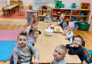 Na zdjęciu widać grupę dzieci siedzących przy stoliku. Na stole znajdują się produkty spożywcze potrzebne do zrobienia ciastek.