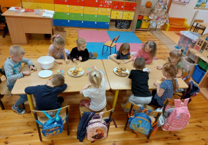 Zdjęcie przedstawia dzieci siedzące przy stolikach i ozdabiające ciasteczka kolorowym lukrem.