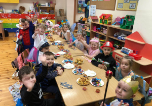 Na zdjęciu widać dzieci siedzące przy stolikach , na których jest słodki poczęstunek. Każde z nich jest pięknie ubrane, przypominające postać bajkową.