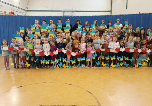 Zdjęcie przedstawia grupę dzieci, które trzymają w rękach papierowe motyle w kolorze niebiesko- żółtym symbolizujące flagę Ukrainy oraz łańcuch z biało- czerwonych serc symbolizujący flagę Polski.