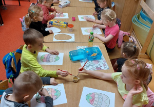 Zdjęcie przedstawia grypę dzieci, które malują jaja wielkanocne na kartonie.