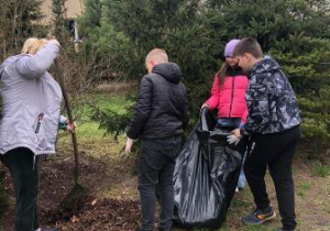 Uczniowie klasy 5 wraz z nauczycielem zaangażowani w prace porządkowe wokół szkoły.