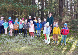 Dzieci wraz z Panią stoją na leśnej polanie.