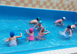 Dzieci pływają z deskami w brodziku.
