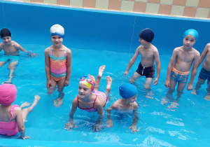 Dzieci ubrani w stroje kąpielowe znajdują się w brodziku z wodą.