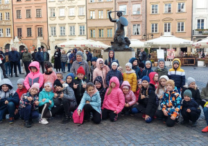 Grupa dzieci przy pomniku Syrenki Warszawskiej.