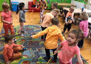 Dzieci tańczą z pomarańczowymi wstążkami.