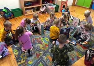 Dzieci siedzą na dywanie. Odpakowują prezenty.