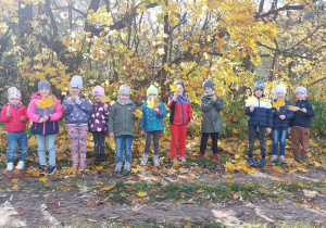 Dzieci stoją przy drzewie w kolorach jesieni.